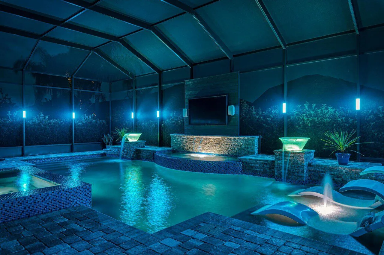 Blue LED pool cage with spa, TV wall, and stone waterfall features