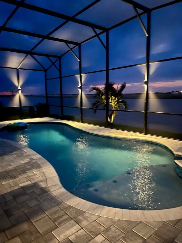 Twilight pool cage lighting with lake view and palm trees