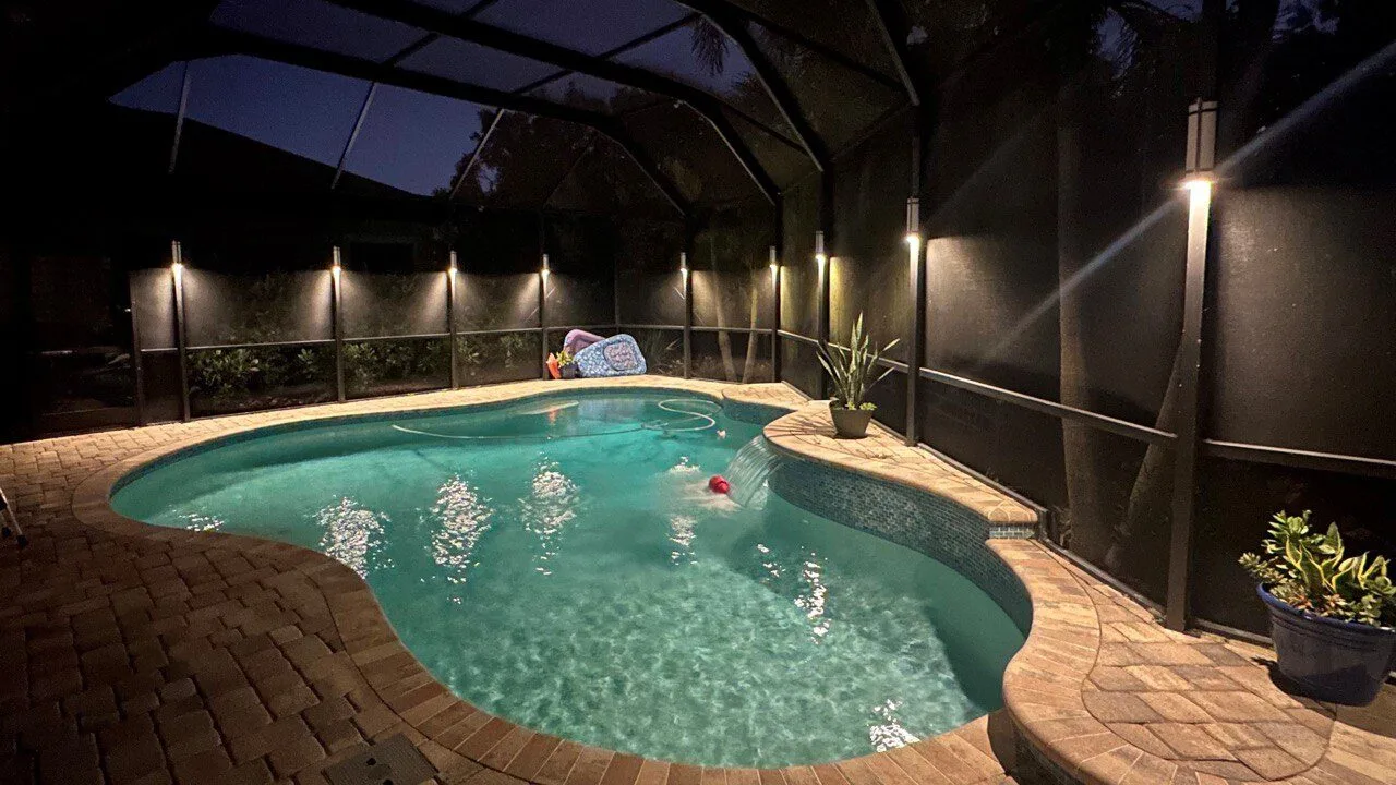 Warm white pool cage lighting in a cozy residential setting with waterfall
